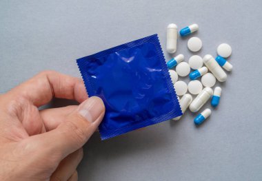 Yakın plan bir el, mavi bir prezervatif ambalajı içinde haplar ve kapsüller var.