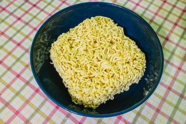 Koyu mavi tabakta pişmemiş hazır ramen eriştesi, ekose masa örtüsü.