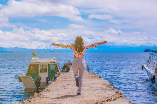 young latin tourist woman with her arms up on a dock on the shor