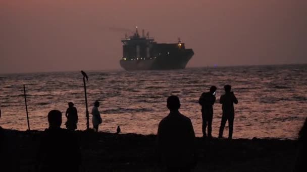 ケララのビーチの背面にシルエット人間と大きな貨物船 — ストック動画