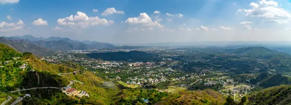 Dehradun şehrinin çarpıcı panoramik manzarası, güzel bir şekilde yüksek bir bakış açısıyla çekilmiş, Himalaya eteklerindeki kentsel yaşam ve doğal manzaraların eşsiz bir karışımını sergiliyor..
