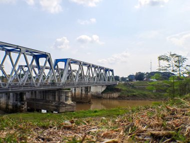 Demiryolu köprüsü, büyük kahverengi nehrin altında, tepenin üzerinden açık mavi gökyüzü.