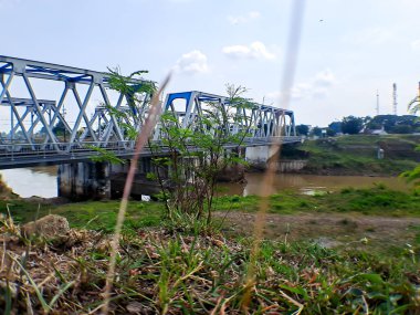 Demiryolu köprüsü, büyük kahverengi nehrin altında, tepenin üzerinden açık mavi gökyüzü.