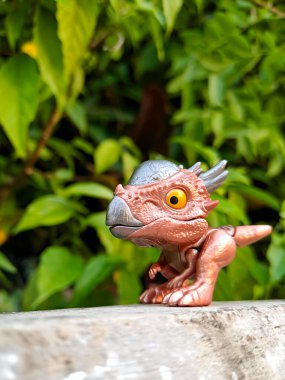 Jurassic World Snap Squad dinozor oyuncağı, metalik aksanlı kahverengi, yeşil yapraklara karşı