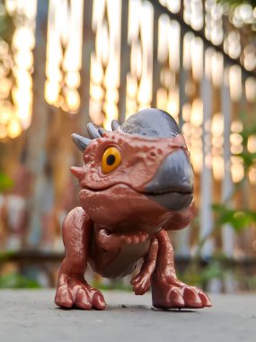 Jurassic World Snap Squad dinozor oyuncağı, metalik aksanlı kahverengi, yeşil yapraklara karşı