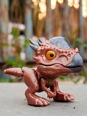 Jurassic World Snap Squad dinozor oyuncağı, metalik aksanlı kahverengi, yeşil yapraklara karşı