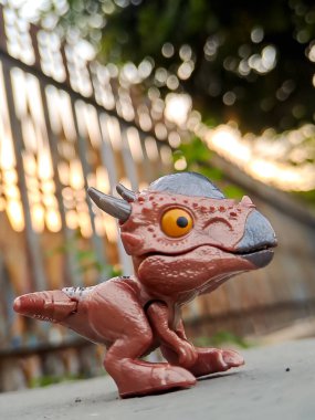 Jurassic World Snap Squad dinozor oyuncağı, metalik aksanlı kahverengi, yeşil yapraklara karşı