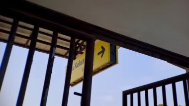 Bu 4K videosunda, paslı metal çubuklar tarafından çerçevelenmiş açık mavi gökyüzüne karşı sarı bir çıkış işareti yer alıyor. Görüntü, şehir veya sanayi temalı projeler için mükemmel bir perspektif ve derinlik hissi yaratıyor.