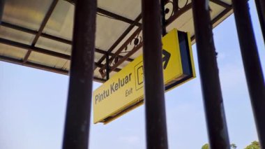 Bu 4K videosunda, paslı metal çubuklar tarafından çerçevelenmiş açık mavi gökyüzüne karşı sarı bir çıkış işareti yer alıyor. Görüntü, şehir veya sanayi temalı projeler için mükemmel bir perspektif ve derinlik hissi yaratıyor.