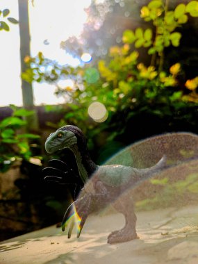 Canlı görünümlü bir dinozor oyuncağını gösteren bir makro çekim. Canlı yeşillik içeren ahşap bir yüzeye tünemiş. Görüntü tarih öncesi bir mucizeyi çağrıştırıyor.