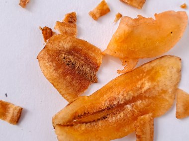 Düz beyaz bir arkaplanda sunulan üç kurutulmuş muz diliminin fotoğrafı. Dilimler, kurutma işleminden görülebilir dokusu olan zengin, altın-turuncu bir renk sergiliyor. Muzun içindeki doğal şekerler karamelize olmuş.