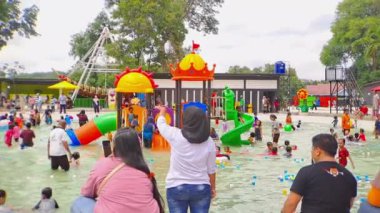 Magetan, Endonezya - 5 Ocak 2024 Bir aile yaz tatili sırasında renkli bir çocuk havuzuna su sıçratır ve güler, unutulmaz anılar yaratır. Seyahat videoları ve aile tatili için mükemmel.