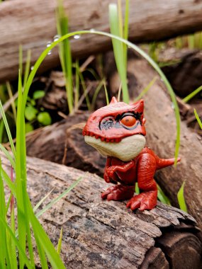 red dinosaur toy peeking through tall grass clipart