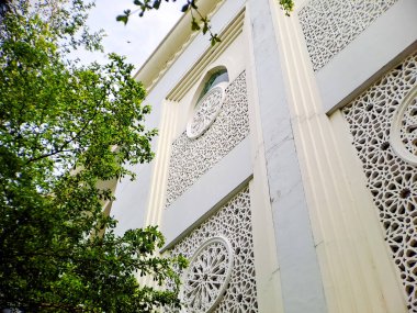 Beyaz bir bina duvarındaki karmaşık İslami mimari detaylar, geometrik desenler ve dairesel bir roset penceresi içeriyor