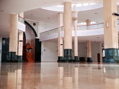 Yüksek tavanı, mermer sütunları ve parlak zemini olan büyük bir cami manzarası huzur ve maneviyat hissi yaratıyor.