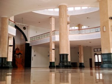 Yüksek tavanı, mermer sütunları ve parlak zemini olan büyük bir cami manzarası huzur ve maneviyat hissi yaratıyor.