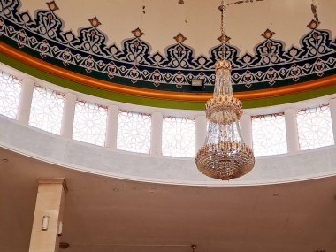 Kristal avize, karmaşık İslami motiflerle boyanmış bir kubbe tavanının altında zarif bir şekilde asılı duruyor. Bir camide huşu ve maneviyat duygusu yaratıyor.