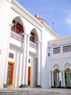 Kırmızı kiremit kaplı görkemli beyaz camii, açık mavi gökyüzüne karşı karmaşık mimari detaylarını sergiliyor.