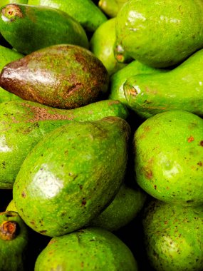 Olgun avokado yığını, canlı yeşil renklerini ve pürüzsüzlüklerini sergiliyorlar.