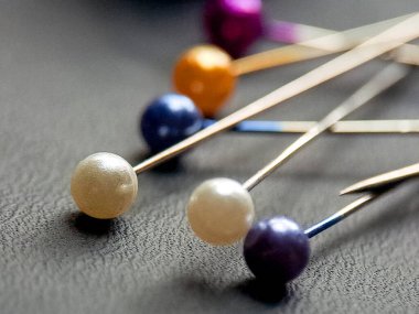 Renkli dikiş iğneleri desenli bir yüzeye dayanır. Renk ve metalik parlaklığa odaklı çarpıcı bir düzenleme oluşturur. Yaratıcılık ve işçiliği çağrıştırır.