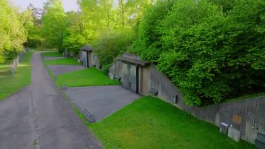 Mühimmat deposu, güçlendirilmiş beton duvarlar ve asfalt yol boyunca uzanan çimenli yamaçlarla bir orman bölgesinde duruyor.