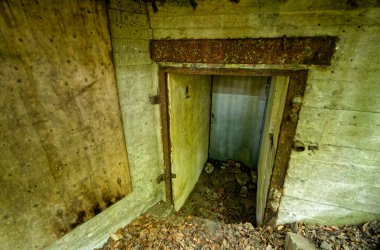 Terk edilmiş 2. Dünya Savaşı beton sığınak girişi paslı metal kapı ve çatlak duvarlar, tarihi savaş zamanı askeri yapısı