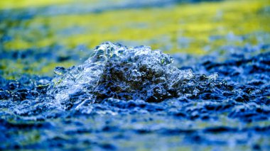 Su damlacıkları / su birikintisi ve güneş ışığı yansımaları. Güneşin altındaki bir derede küçük su damlalarındaki renklerin muhteşem oyunu. Yakından çekilen gün ışığında kıyıda.