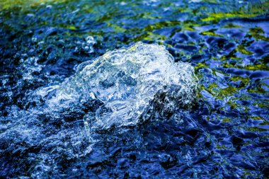 Su damlacıkları / su birikintisi ve güneş ışığı yansımaları. Güneşin altındaki bir derede küçük su damlalarındaki renklerin muhteşem oyunu. Yakından çekilen gün ışığında kıyıda.