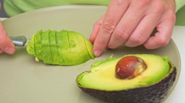 Kadın avokado keser. Evdeki yeşil tabakta avokado dilimleyen kadının yakın çekimi. Vejetaryen gıda konsepti. E vitamini, avokado yağı ve antioksidan. Bilinçli beslenme kavramı.