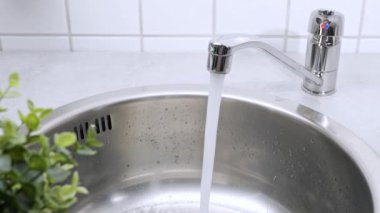 Mutfaktaki musluktan paslanmaz çelik lavaboya temiz su akıntısı akıyor. Çevre, su kirliliği ve su kıtlığı kavramı