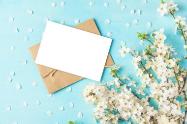 Blank wedding greeting card or invitation with spring blossom cherry flowers on pastel blue background. Mock up. Flat lay