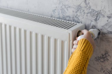 Male hand in yellow sweater adjusting comfort temperature in home by control gas heater. Energy efficiency or economy in winter concept