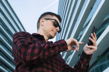 Modern ofis binalarının dışında cep telefonu ya da akıllı telefon cihazı kullanan genç bir serbest çalışan ya da güneş gözlüğü uzmanı. Telefonlu hippi.