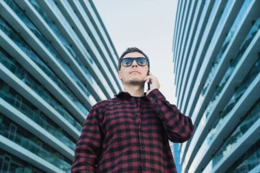 Modern ofis binalarının dışında güneş gözlüklü, cep telefonu ya da akıllı telefon kullanan bir bilişim uzmanının portresi. Komik atış.