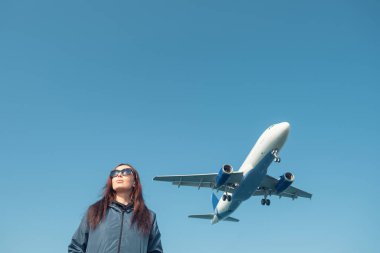 Güneş gözlüklü, alçaktan uçan bir uçak ya da mavi gökyüzüne karşı uçan bir uçağın portresi. Kadın turistin üzerine uçak iniyor. Seyahat kavramı