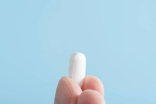 Mężczyzna Trzyma Białą Pigułkę Palcach Niebieskim Tle Antybiotyk Lub Lek — Zdjęcie stockowe