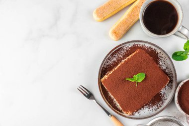 Kahve fincanı ve çatalla geleneksel İtalyan tatlı tiramisusu. Beyaz masada taze naneli ev yapımı tiramisu kek porsiyonu. Kopyalama alanı olan üst görünüm. Lezzetli yemek.