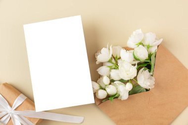 Beyaz yasemin çiçekleri ve bej arka planda hediye kutusu olan boş bir tebrik kartı. Düğün davetiyesi. Model yap. Düz yatıyordu. Anneler Günü düzeni