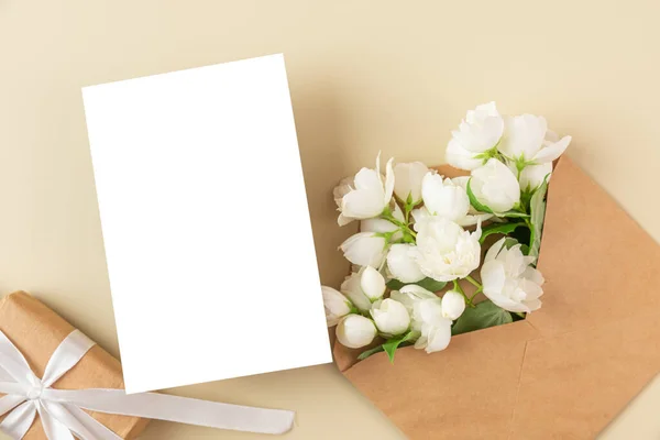 stock image Blank greeting card with white jasmine flowers and gift box on beige background. Wedding invitation. Mock up. Flat lay. Mothers day layout