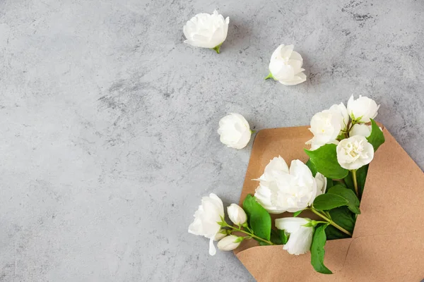 Stock image White jasmine flowers in paper envelope on gray background. Flat lay. Wedding invitation. Festive layout. Top view