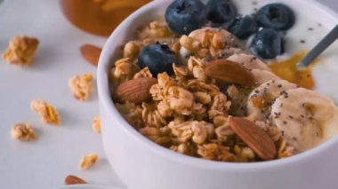 Sağlıklı kahvaltı için beyaz zemin üzerinde yuladan yapılmış yoğurt, yulaf, yabanmersini, chia tohumu, bal ve fındık. Diyet yemek.