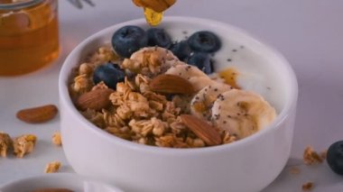 Yulaf ezmeli, muzlu, yabanmersinli, fındıklı, chia tohumlu Yunan yoğurdu kasesine bal dök. Sağlıklı kahvaltı.