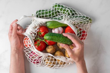Erkekler, organik sebze ürünleriyle birlikte alışveriş torbalarından salatalık alıyor. Çevre dostu ağ tüccarı. Plastiksiz konsept. Üst görünüm