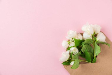 Beyaz yasemin çiçekleri pembe arka planda kağıt zarf içinde. Düz yatıyordu. Düğün davetiyesi. Şenlik düzeni. Üst görünüm