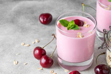 Vişneli yoğurt ya da bardakta yoğurt taze böğürtlen, yulaf ezmesi, gri arka planda sağlıklı kahvaltı için nane şekeri. Lezzetli yemek.