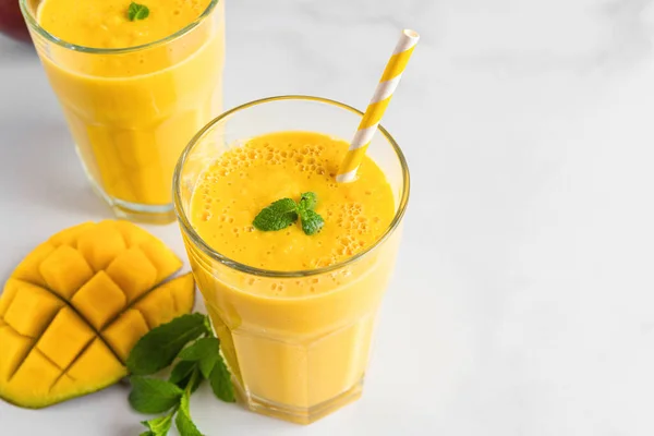 stock image Fresh yellow mango smoothie in glasses with straw, fresh fruits and mint. Summer tropical drink on white background with copy space