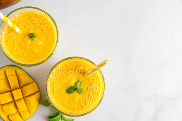 stock image Mango smoothie in glasses with mint, fresh fruits and straw. Summer tropical drink on white background. Top view with copy space