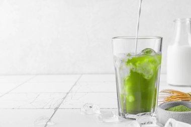 Beyaz arka planda bir bardak buzlu yeşil kibrit lattesine süt ya da krema dökmek. Soğuk yaz içkisi. Sağlıklı detoks içeceği