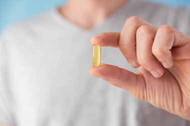 Elinde D vitamini olan kapsüllü bir adam. Balık yağı ile besin takviyesi. Sağlık desteği ve tedavi konsepti. Kapat.