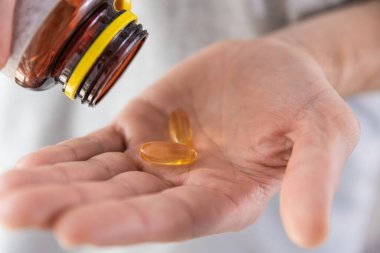 Adam balık yağı kapsüllerini omega 3 ile dolduruyor. İlaç şişesinden D vitamini. Besin takviyesi. Sağlık desteği ve tedavi konsepti. Kapat.